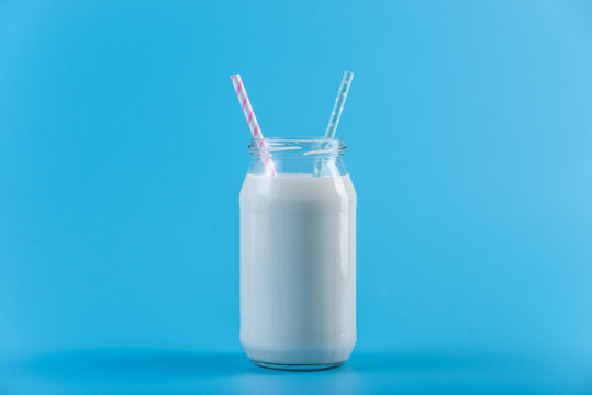 Glass bottle of fresh milk with two straws on blue background. Colorful minimalism. Healthy dairy products with calcium