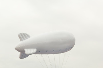Naklejka premium White inflatable dirigible with a place for a logo on a background of a gray sky with clouds. Copy space