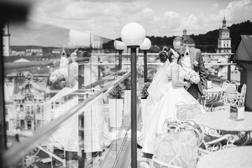 Fashionable newlyweds stand on the roof on a sunny day and enjoy each other. The bride and groom in the background of a large and sunny city.