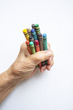 Senior woman's hand holding multicolour crayon  isolated on white background