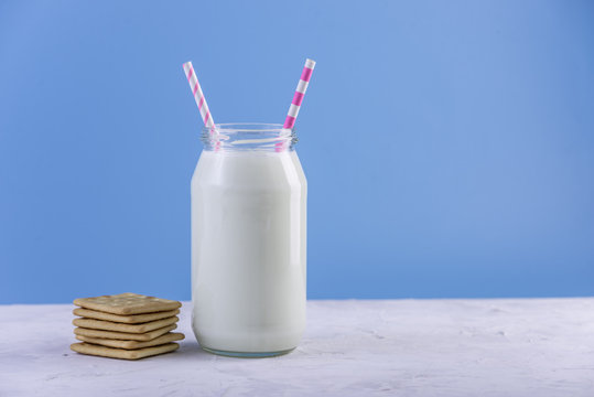 Bottle of fresh milk with straw and cookies on blue background. Colorful minimalism. Healthy dairy products with calcium