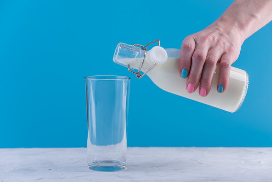 Woman's hand pours fresh milk from a bottle into a glass on a blue background. Healthy dairy products with calcium