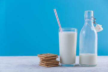 Bottle of fresh milk with straw and cookies on blue background. Colorful minimalism. Healthy dairy products with calcium