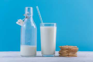Bottle of fresh milk with straw and cookies on blue background. Colorful minimalism. Healthy dairy products with calcium