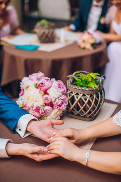 Weddings bride and groom hold hands. On the wooden table is a bouquet of the bride. Wedding day in summer. Newlyweds in outdoor summer cafe. Wedding photossesion.