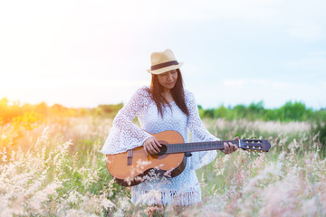 Woman playing the guitar in meadow. travel and sunset, soft and select focus
