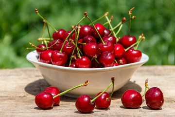 Bowl with fresh cherry on rustic wooden table outdoor