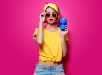 Girl in sunglasses and yellow t-shirt holding a blue cup of coffee on pink background