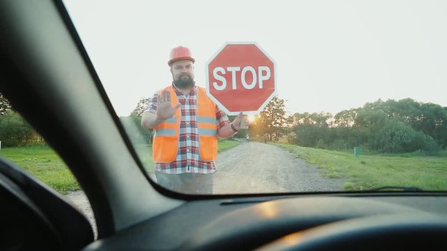 A construction road worker stopping traffic, holding a stop sign. View from the car