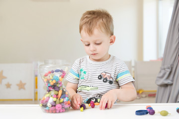 A little boy is playing with beads and other small toys. Pastime in the children garden or play center