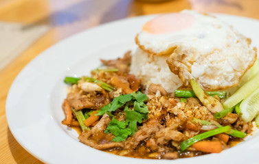 delicious Thai food garlic and pepper with pork and Fried egg with jasmin rice closeup with carrot cucumber Spring onion and coriander leaves on top in white plate .delicious Thai food