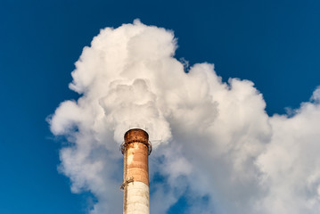Tall grungy factory pipe emitting thick white fume against cloudless blue sky