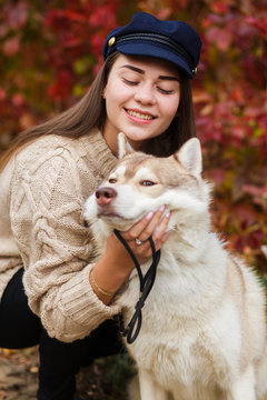 young woman in casual clothes with her white Samoyed husky dog posing for a picture with closed eyes in autumn Park. Vertical portrait