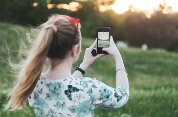 girl is photographing the sunset on the phone back view