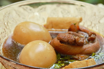boiled egg with pork leg in herb brown soup on glass bowl