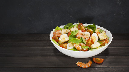Shrimp salad with salad, arugula, quail eggs, cherry tomatoes, olive oil and balsamic vinegar on a wooden table. Caesar salad with shrimp.