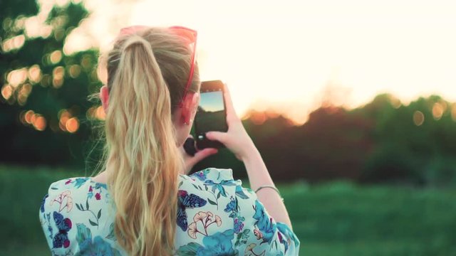 girl is photographing the sunset on the phone back view slow mo