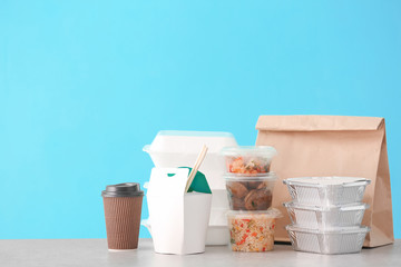 Different packages with delicious food on table against color background. Delivery service