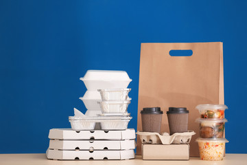Different packages with delicious food on table against color background. Delivery service