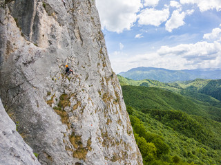 Rock climbing. Climber climbing on the cliff of the mountain wit the forest and cloudy sky in the background. Alpine climbing on the rocky mountains. Extreme climbing. Escalating the mountain.