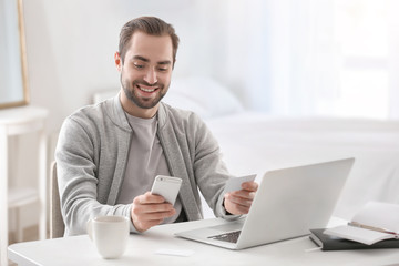 Male freelancer with smartphone and business card at workplace