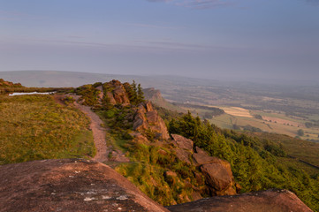 Sunset lights the trees, heather and rocks at the Roaches, Staffordshire in the Peak District National park. Hen Cloud can be viewed in the distance.