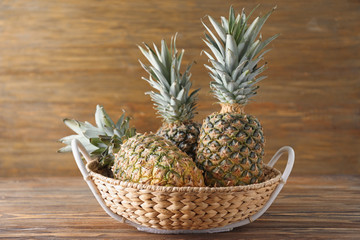 Tasty pineapples in basket on wooden table