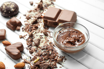 Different tasty candies and bowl with melted chocolate on white wooden table