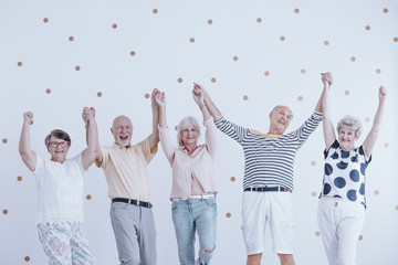 Group of active elderly people holding hands up and enjoying meeting