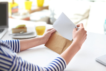 Young woman putting letter into envelope at table in cafe. Mail delivery