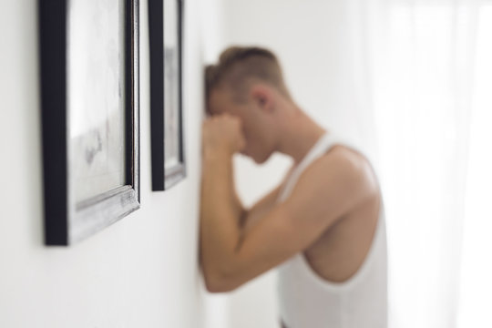 Pensive young man with face against wall