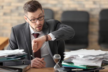 Businessman looking at his wristwatch at table in office. Time management concept