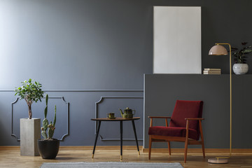 Red armchair between pink lamp and table in grey living room interior with copy space. Real photo