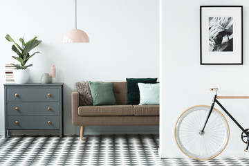 Chest of drawers next to a sofa with pillows, patterned floor in a living room interior with a bike...