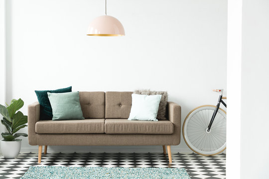 Modern sofa with green pillows under a pink lamp, bike and plant set in a living room interior