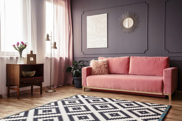 Side angle of a living room interior with a powder pink sofa, patterned rug, wooden cabinet and wall decorations