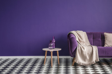 Dark purple sofa with a blanket beside a small table with bottles standing on black and white...