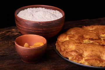 A bowl with flour and apricot cake on a wooden background