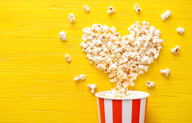 Paper bucket and heart made of tasty popcorn on color wooden background - obrazy, fototapety, plakaty