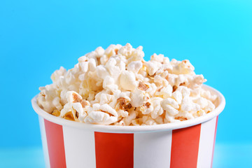 Paper bucket of tasty popcorn on color background, closeup