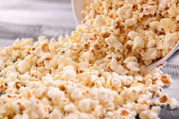 Paper bucket with scattered tasty popcorn on table, closeup