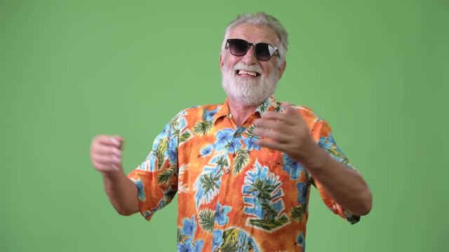 Handsome senior bearded tourist man ready for vacation against green background