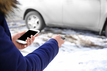 Young woman with phone using car alarm outdoors