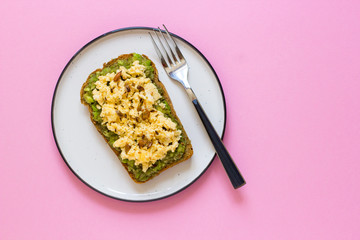 Egg on whole wheat bread with avocado, pink background top view