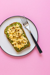 Egg on whole wheat bread with avocado, pink background top view