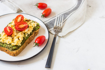 Scrambled eggs on whole wheat bread with avocado and cherry tomatoes