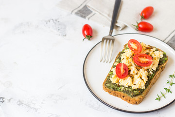 Scrambled eggs on whole wheat bread with avocado and cherry tomatoes