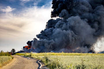 Building fire among fields and huge black smoke cloud