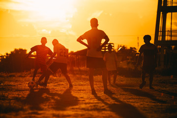Fototapeta na wymiar Silhouette action sport picture of a group of kids playing soccer football for exercise in community rural area under the sunset.