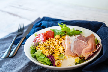 Salad with fusilli pasta accompanied tomatoes, mozzarella, smoked ham and italian cheese